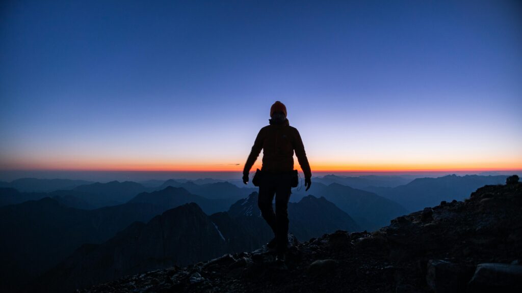 Silhouette of a hiker on a mountain peak during a stunning sunrise, capturing the essence of adventure.